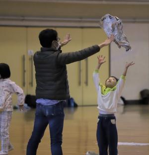 保護者が高いところから落とした新聞紙をキャッチしようとする男の子の写真