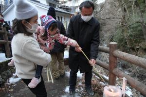 抱きかかえられた子どもが支えられながら氷灯ろうに火を灯す様子の写真