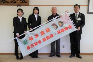 丸子地域自治センター長、木曽義仲信州丸子会副会長、学生がのぼり旗を持つ写真